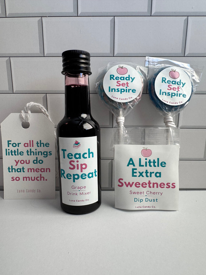 A gift set from Little Candy Co. featuring a bottle of Grape Sip Repeat grape drink mix, a bag of A Little Extra Sweetness Dip Dust, and two lollipops labeled Ready Set Inspire, displayed against a white subway tile background.