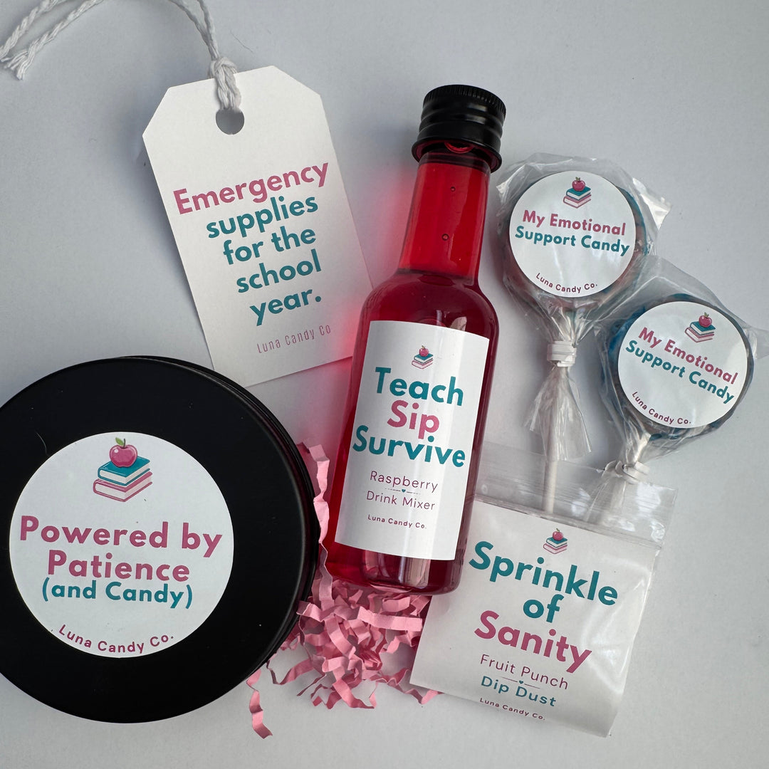 A curated gift set on a light gray background featuring a small bottle of raspberry drink mixer, a black tin of fruit dip dust, two lollipops, and paper tags with playful school-themed messages. The brand &