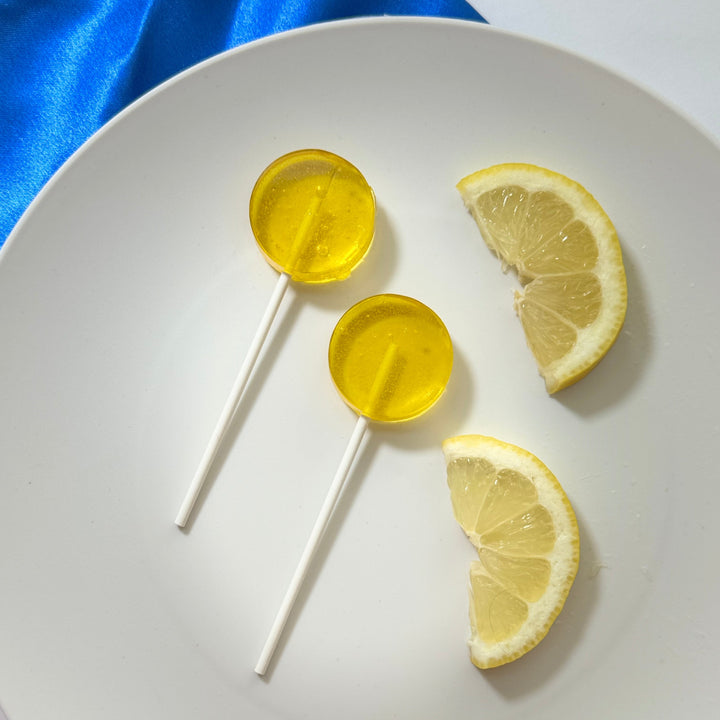 Two lemon slices and two yellow lollipops on a white plate with a blue cloth background.