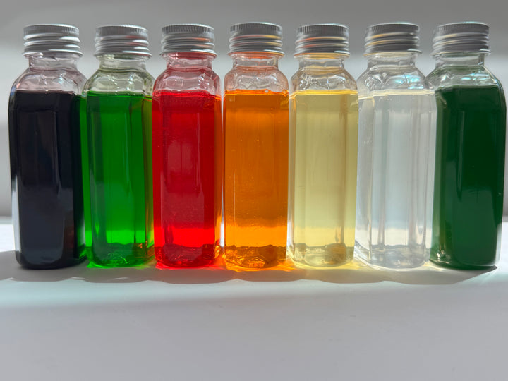 Row of small drink syrup bottles with silver caps containing different colored liquids on a white background